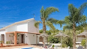 Eine weiße Villa mit einem Ziegeldach, einem Swimmingpool und Palmen im Hintergrund.