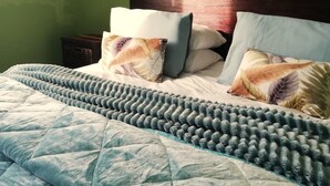 Ein Bett mit einer gesteppten Decke, zwei Kissen mit Federmotiv und einem dunklen Kopfteil.