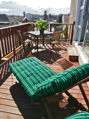 A wooden deck with a green-striped bench, a table with chairs, and a potted plant. - Dawson's Creek Muizenberg (Cape Town)