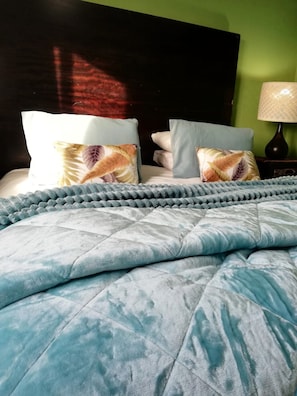 A bed with a blue quilt and pillows, a dark headboard, and a green wall. - Dawson's Creek Muizenberg (Cape Town)