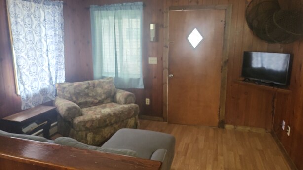 Una sala de estar con piso de madera, un sofá, un televisor montado en la pared y una puerta con ventanal.
