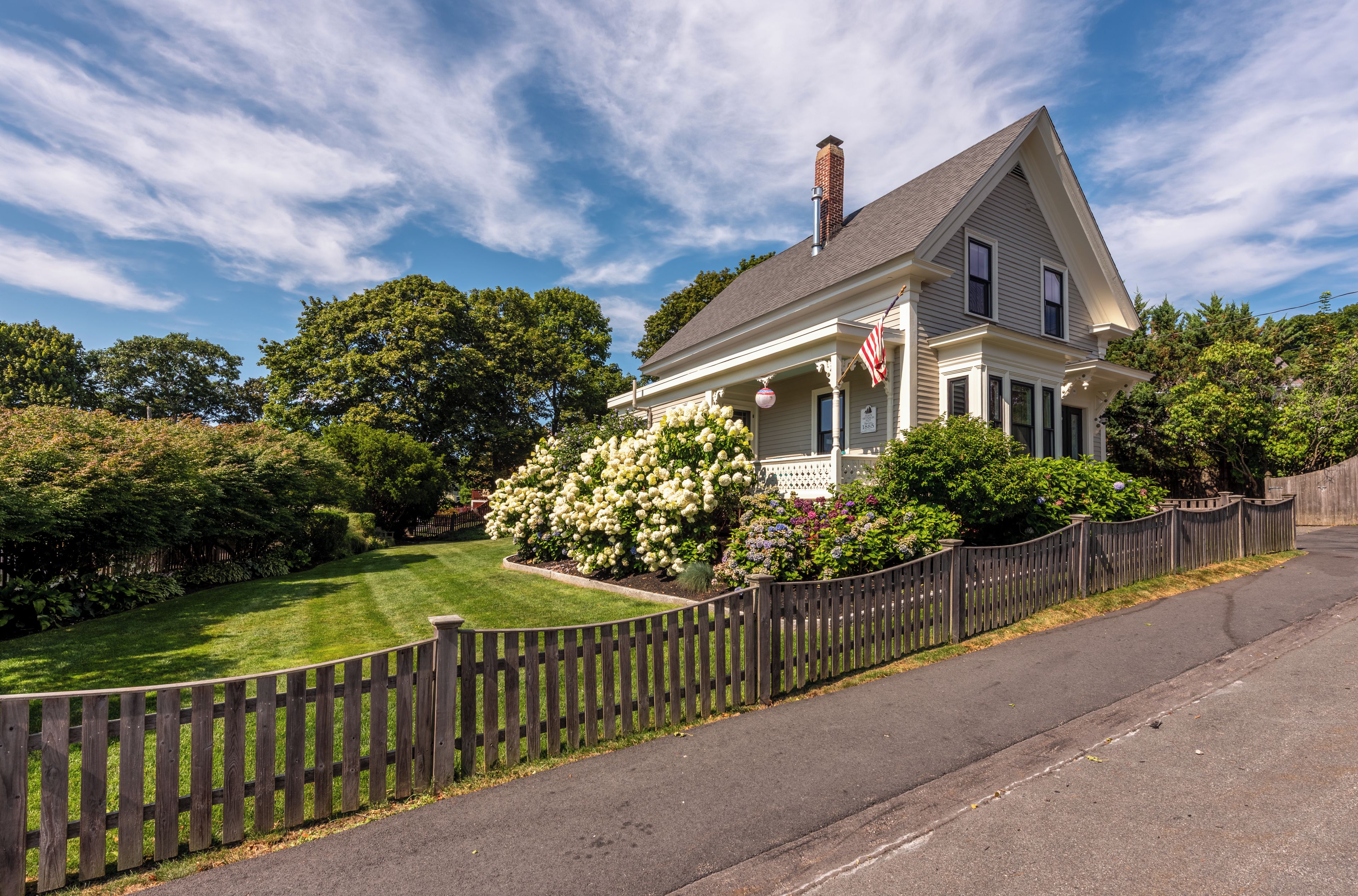 A two-story house with a front porch, a wooden fence, and a well-maintained lawn.