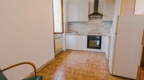 Cocina compacta con armarios blancos, horno integrado y refrigerador.