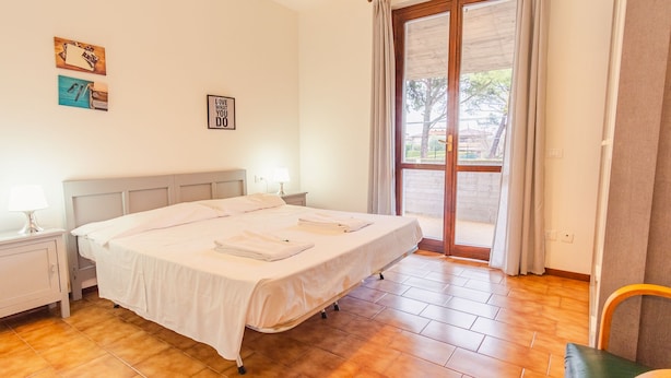 Un lit bien fait, agrémenté d’oreillers et de serviettes, une table de chevet avec une lampe, et une vue sur l’extérieur à travers une porte vitrée.