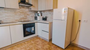 A compact kitchen with white cabinets, a built-in oven, a microwave, and a refrigerator.
