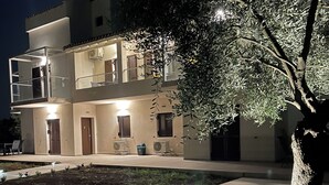 Un edificio de dos pisos con balcones, un árbol en primer plano e iluminación exterior.