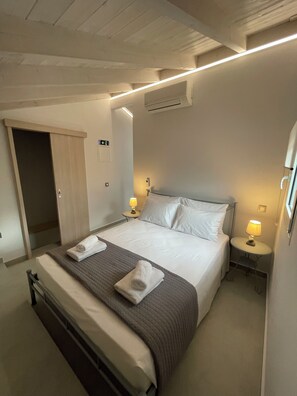 Quarto de hotel com cama, mesas de cabeceira, abajur, unidade de ar condicionado e uma porta.