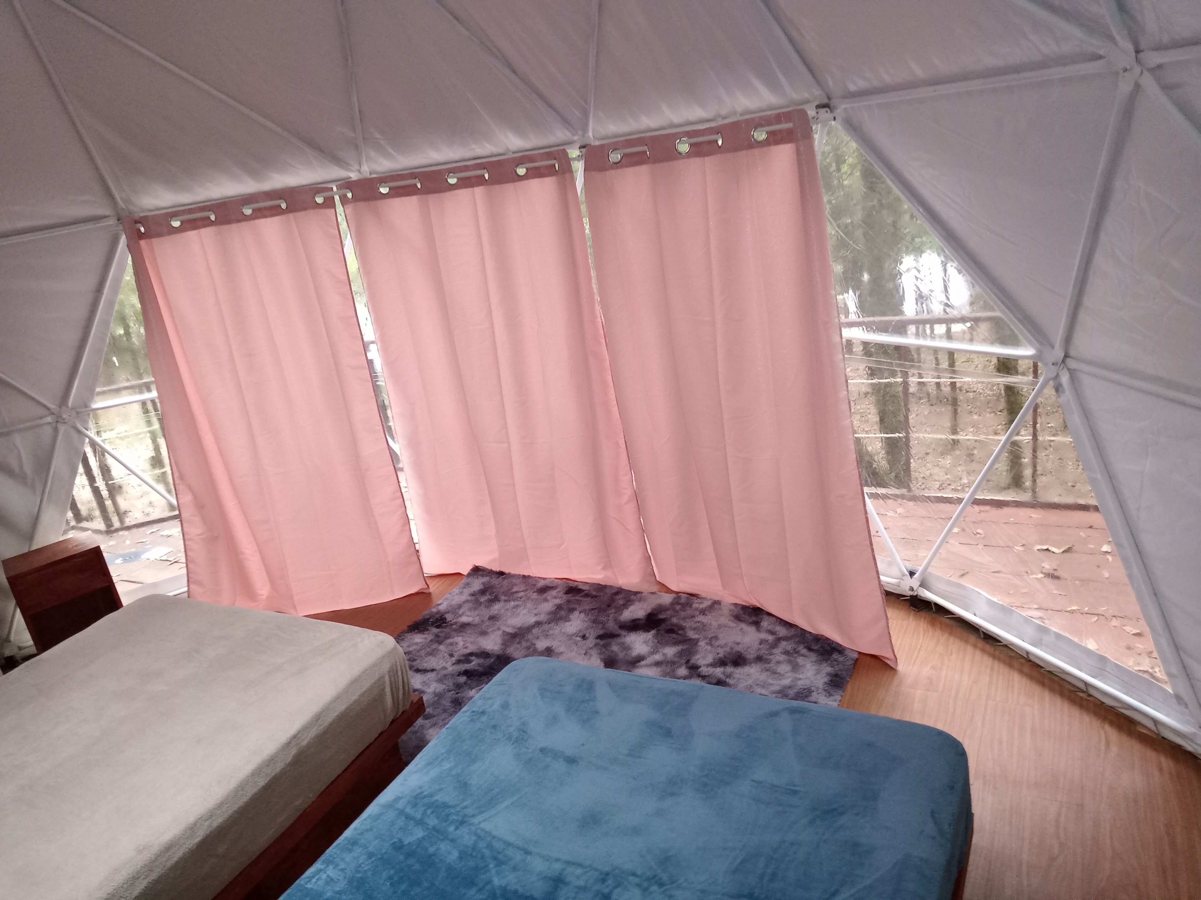 Una tenda con due letti, tende rosa e vista sull'esterno.