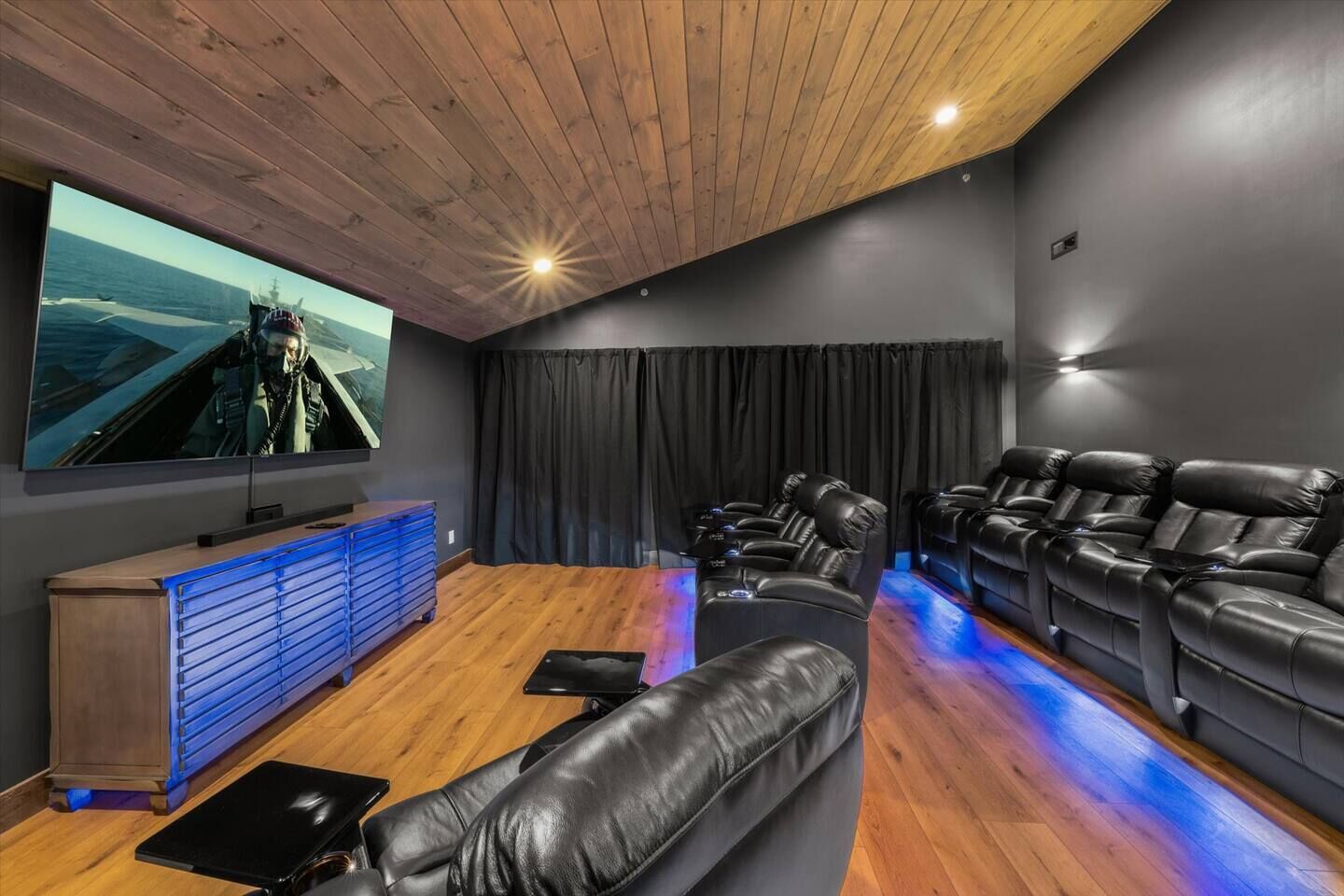 Ein modernes Heimkino mit einem großen Flachbildfernseher, bequemen Ledersesseln, einem Holzschrank und einem blau beleuchteten Boden.