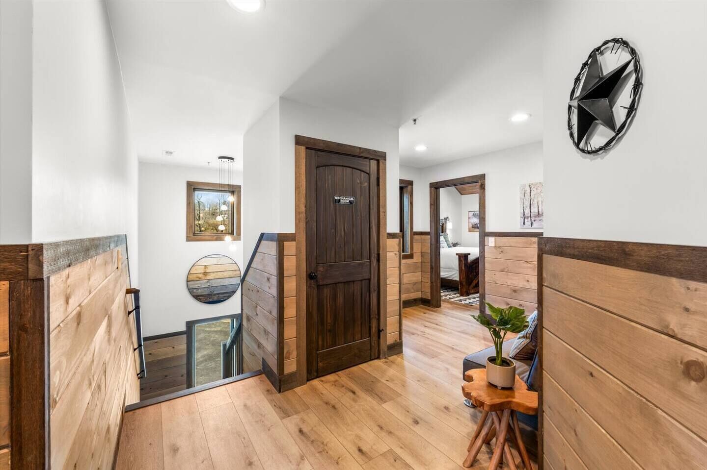 A hallway with wooden walls and floors, a dark wooden door, and a round mirror on the wall.