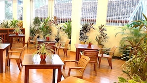 Un espace repas avec des tables et des chaises en bois, entouré de plantes en pot.