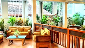 Un espace de détente intérieur accueillant, avec un canapé, des fauteuils et une table basse, entouré de plantes en pot et d’une rambarde en bois.