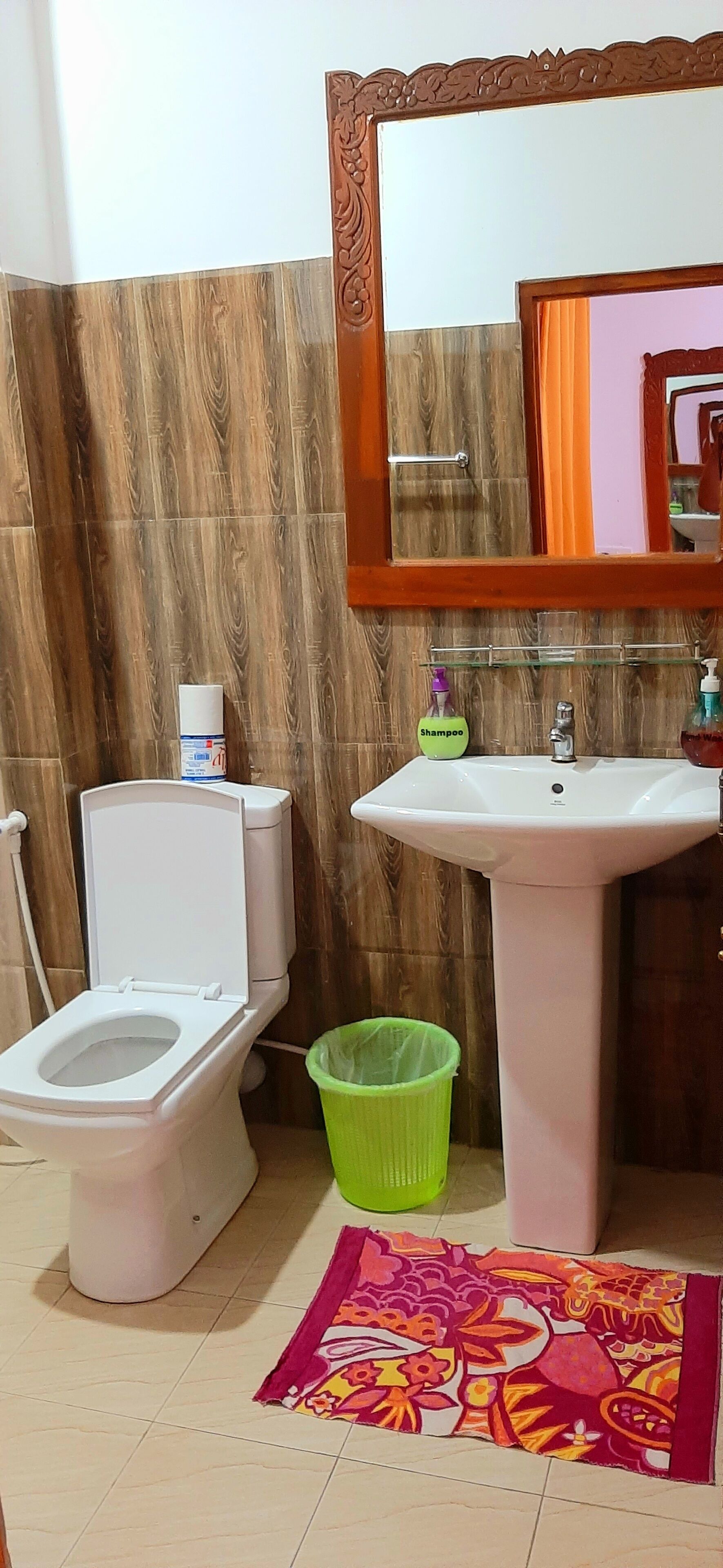 A bathroom with a toilet, sink, mirror, and a green trash bin.