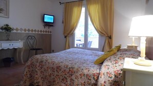 Une chambre à coucher avec un lit, un bureau, une chaise, un téléviseur et une fenêtre avec des rideaux.