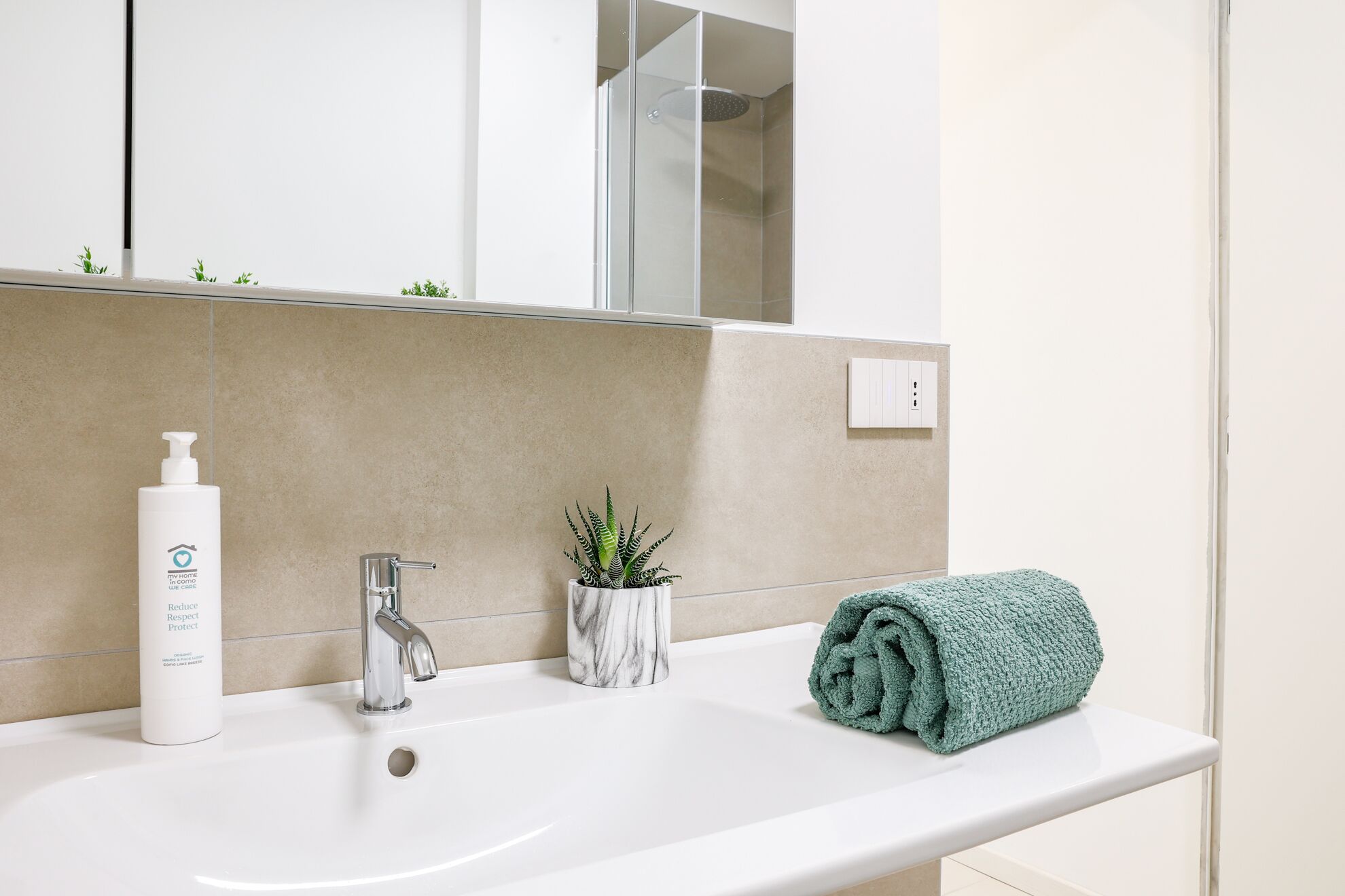 Une salle de bain avec un lavabo blanc, un miroir, une douche et une serviette.