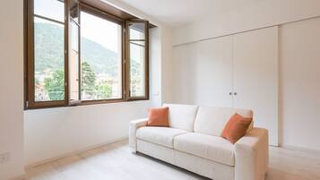 A room with a large window, a white sofa with two cushions, and a wardrobe.