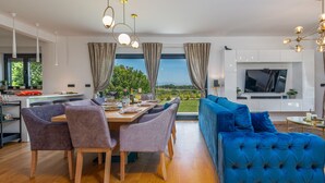 Una sala de estar moderna con un sofá azul, un comedor con mesa y sillas de madera, y una zona de cocina con un televisor y armarios.