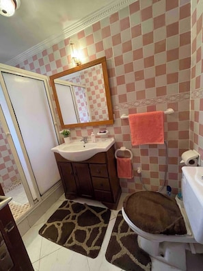 Ein Badezimmer mit Schachbrettmuster an der Wand, einem Waschbecken, einem Spiegel, einer Toilette und einer Duschkabine.
