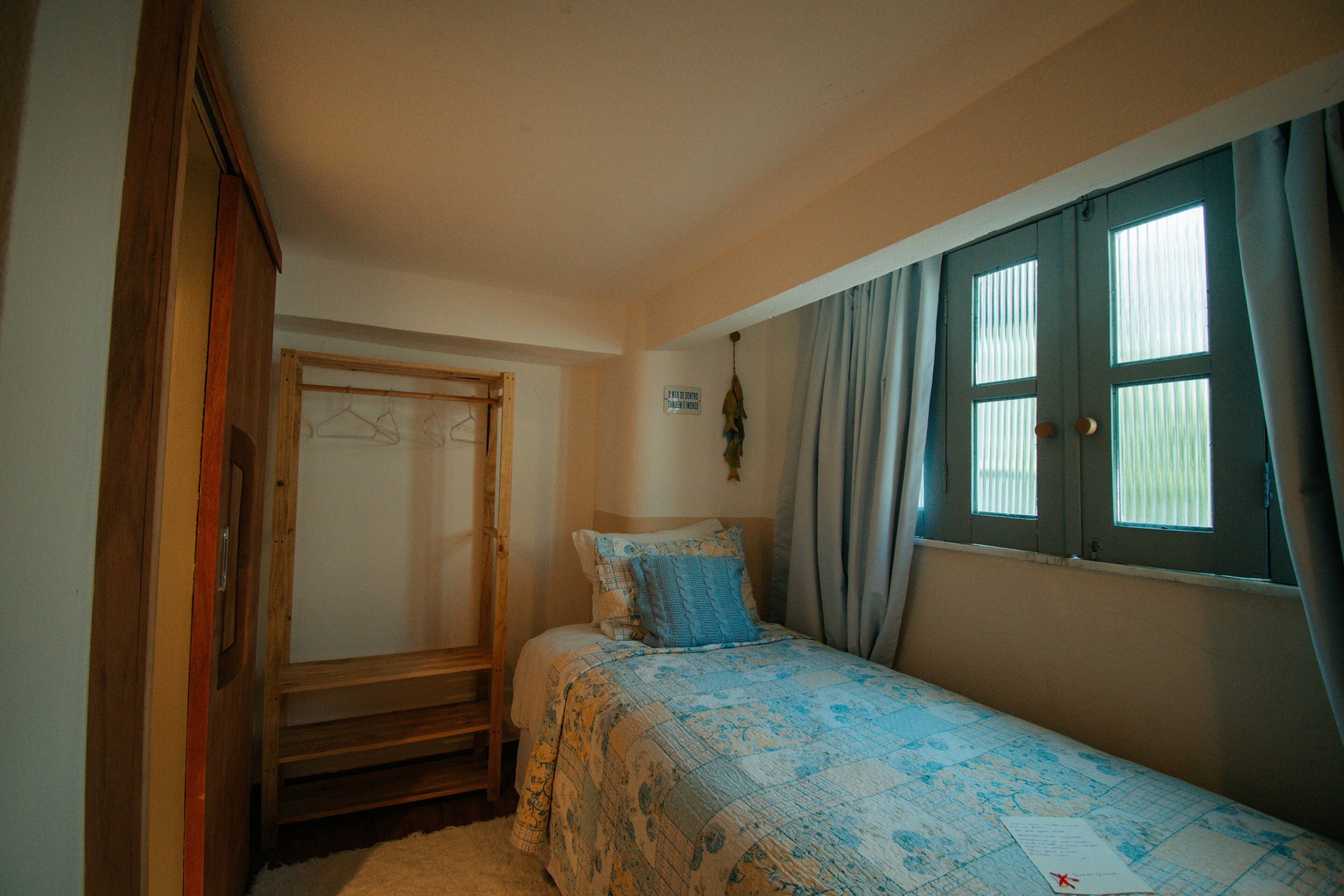 A bedroom with a bed, a wooden wardrobe, a window with curtains, and a map on the bed.