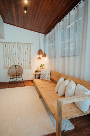 A cozy room with a wooden bench, a woven chair, and a bed with pillows. - Pousada Girassol Morro (Cairu)