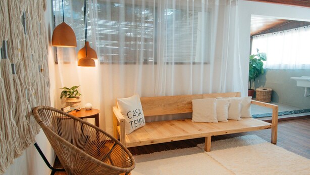 A modern living room with a wooden ceiling, a woven chair, a wooden sofa with cushions, and a white rug. - Pousada Girassol Morro (Cairu)