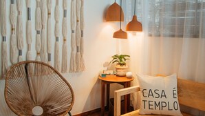 A cozy room with a wooden ceiling, a woven chair, a wooden bench with a cushion, a small table with a plant, and a wall hanging. - Pousada Girassol Morro (Cairu)
