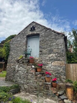 A stone building with a single door and windows, surrounded by greenery and potted plants. - Murlough Country House built in 1750 (Dundrum)