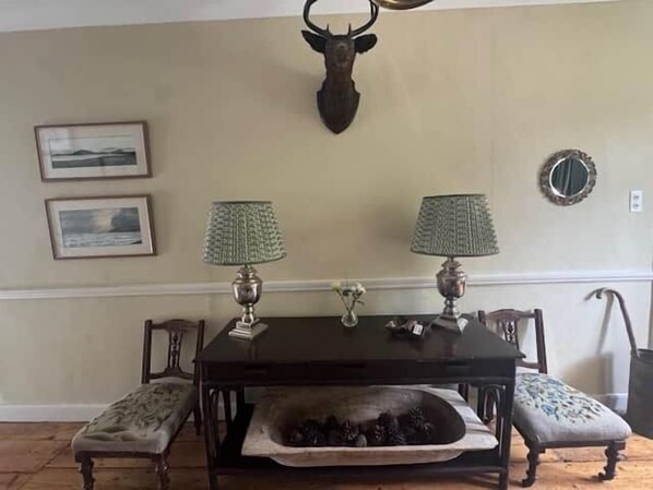 Un comedor con una mesa, dos lámparas, una cabeza de ciervo montada en la pared y cuadros enmarcados.