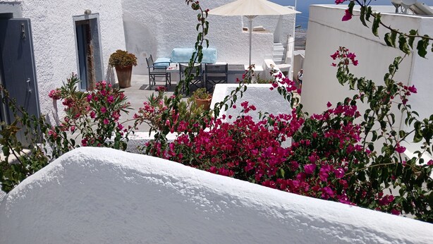 A white-walled building with a patio area featuring a table and chairs, a potted plant, and a white umbrella. - Authentic Castle House in Santorini(sleeps 5) (Pyrgos Kallistis)