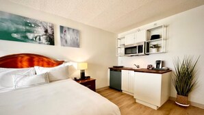 A hotel room with a bed, a bedside table, a lamp, a small kitchen area with a microwave, and a potted plant. - King Studio Suite with Kitchenette in the heart of Racine! (Mount Pleasant)