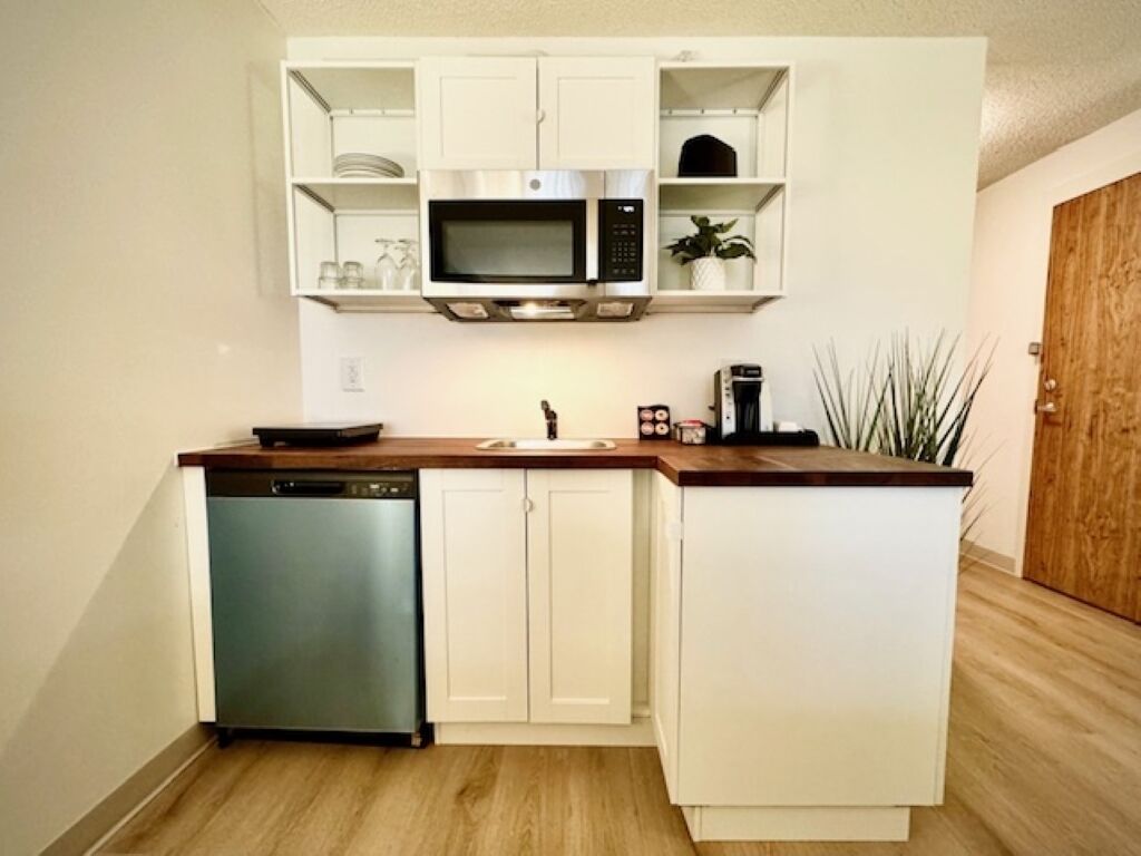 A compact kitchen with white cabinetry, a built-in microwave, a dishwasher, and a coffee maker.
