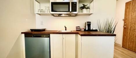 A compact kitchen with white cabinetry, a built-in microwave, a dishwasher, and a coffee maker.
