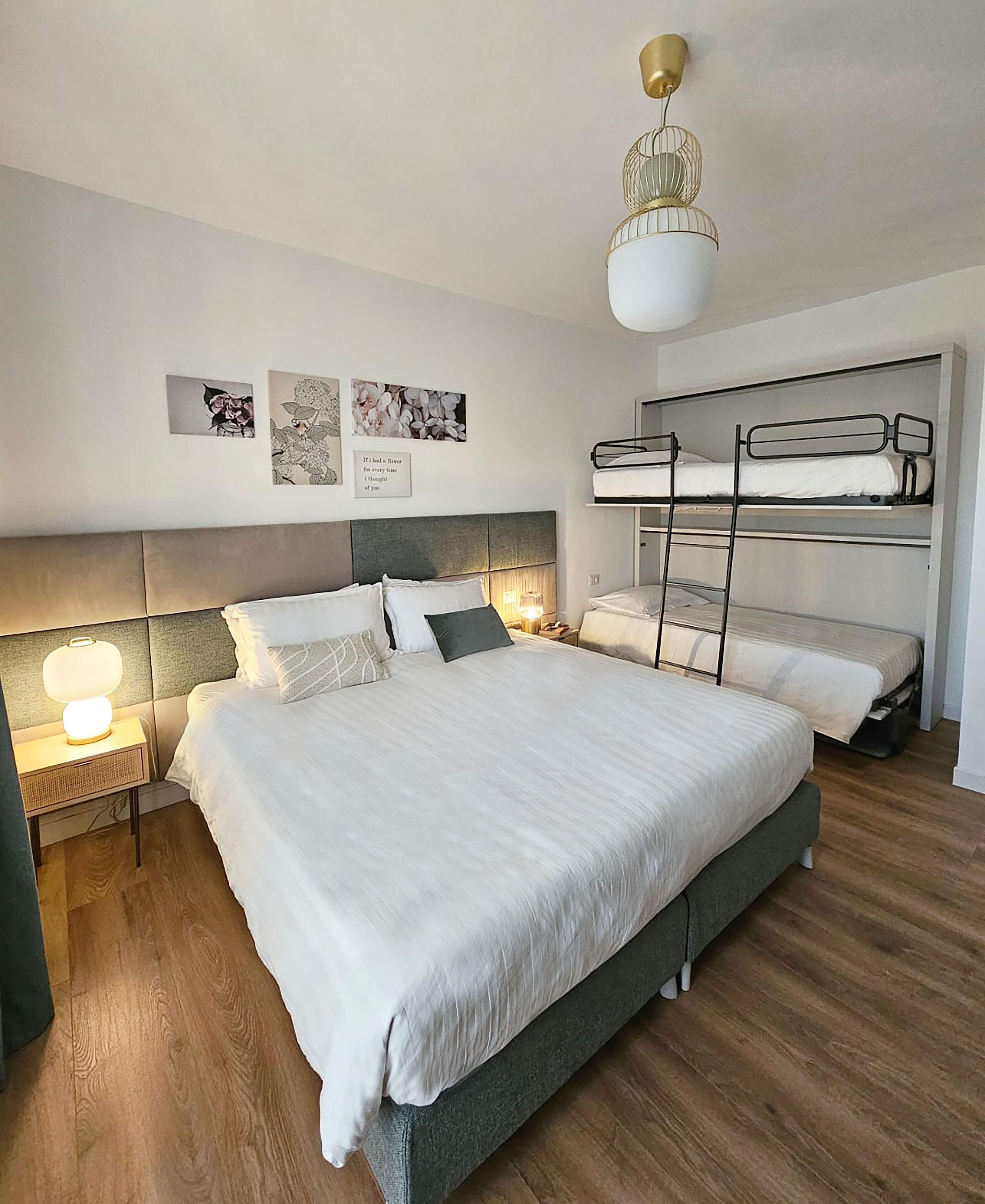 A modern bedroom with a large bed, bunk beds, and a bedside lamp.