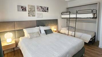 A modern bedroom with a large bed, bunk beds, and a bedside lamp.