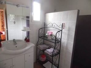 Une salle de bain avec un lavabo blanc, un miroir, une étagère avec des serviettes et une fenêtre.