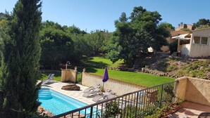 A swimming pool with lounge chairs and a stone wall, surrounded by greenery and trees.
