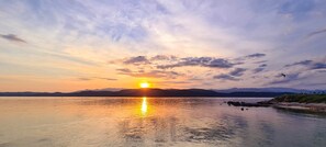 Un coucher de soleil sur une étendue d'eau calme, avec des montagnes en arrière-plan.