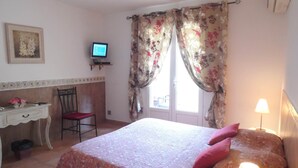 A bedroom with a bed, a desk, a chair, a television, and a window with curtains.