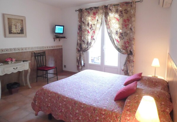 Une chambre à coucher avec un lit, un bureau, une chaise, une télévision et une fenêtre avec des rideaux.