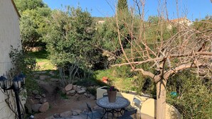 A patio with a round table and chairs, a wooden bench, and a small garden area with rocks and plants.