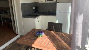 Eine kleine Küche mit weißen Schränken, einer Mikrowelle, einem Kühlschrank und einem Holztisch mit einem Blumenstrauß.