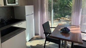 Eine moderne Küche mit Mikrowelle, Kühlschrank und schwarzem Arbeitsplatz. Ein Esstisch mit Stühlen bietet Blick auf einen Garten durch große Fenster.