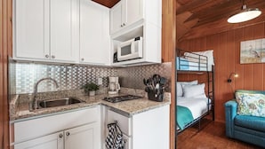 A compact kitchen with white cabinets, a microwave, a sink, and a coffee maker. There is a bunk bed with a blue pillow and a small sofa with a patterned cushion.