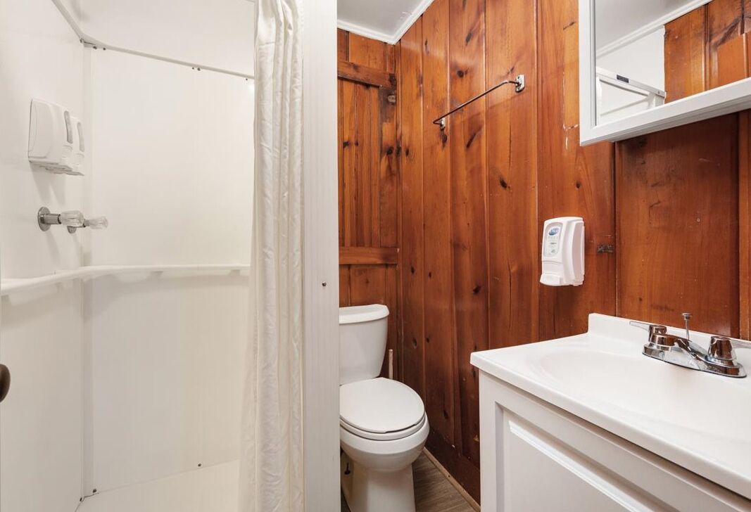 Une salle de bain avec un mur en bois, des toilettes blanches, un lavabo blanc et une serviette accrochée au mur.