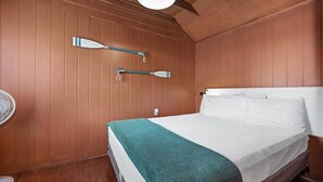 A room with wooden panel walls, a bed with white linens and a teal blanket, and two wall-mounted paddleboards.