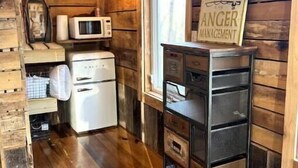 A cozy cabin-style room with wooden walls and floors, a kitchenette with a microwave, a refrigerator, and a sink. There's a television mounted on the wall and a sign that reads "FISHING AGENCE MANAGEMENT". - Fishing Cabin Getaway (Grant)