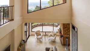 A spacious living area with a high ceiling, a stone fireplace, and a balcony with a view. - House in Boquete, House in Boquete with king beds and hot tub (565749) (Alto Jaramillo)