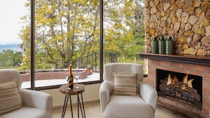 A room with a stone fireplace, two chairs, a small table with a bottle and glass, and a view of trees and mountains. - House in Boquete, House in Boquete with king beds and hot tub (565749) (Alto Jaramillo)