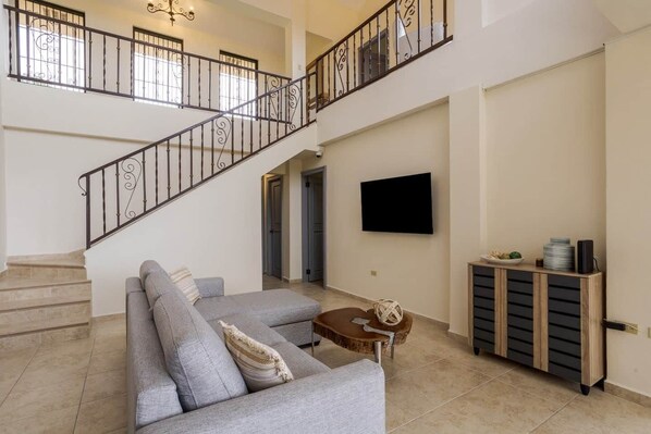 A spacious living area with a grey sofa, a coffee table, a TV mounted on the wall, and a staircase with wrought iron railings. - House in Boquete, House in Boquete with king beds and hot tub (565749) (Alto Jaramillo)