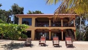 A two-story building with a balcony on the upper floor. There are four lounge chairs in front of the building. - Paradise Beach Belize Suite B (downstairs) (Hopkins)